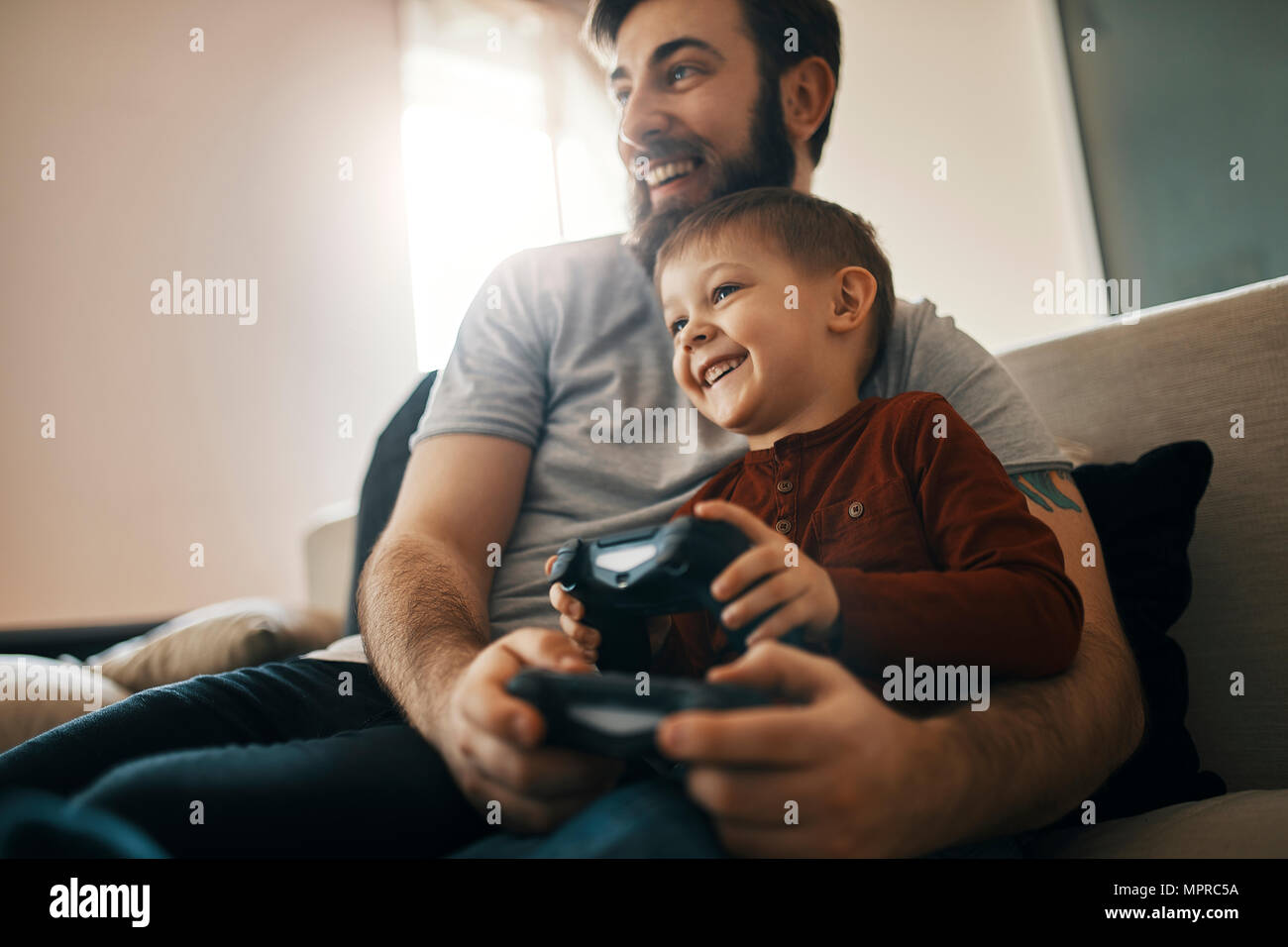 Happy father and little son sitting together on the couch playing computer game Stock Photo