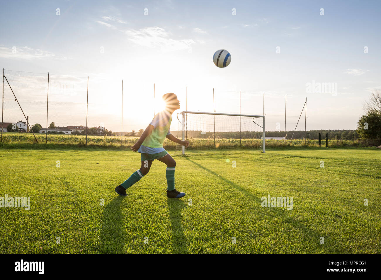 Young football player heading the ball on football ground at sunset Stock Photo