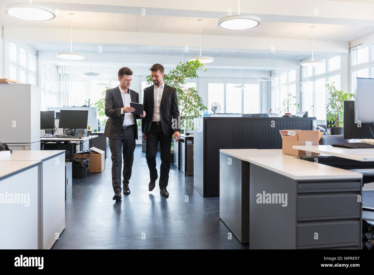 Two businessmen walking in office, using digital tablet, talking Stock Photo