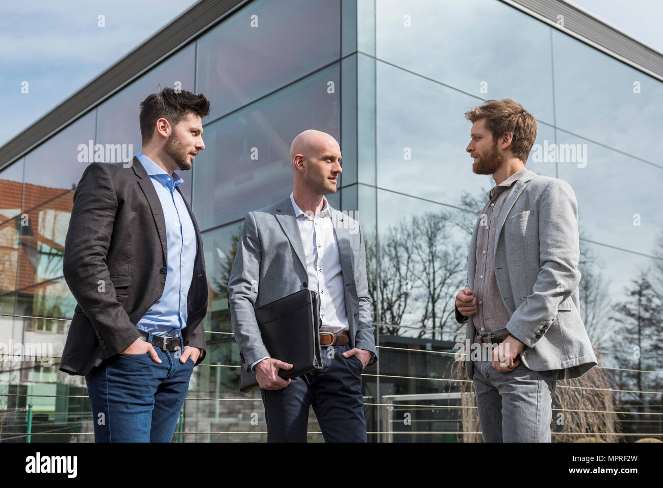 Three businessmen standing outside office building talking Stock Photo