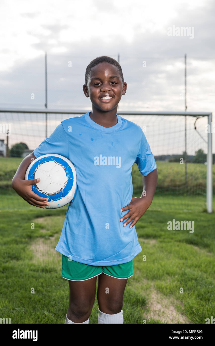 Portrait of smiling young football player holding ball on football ground Stock Photo