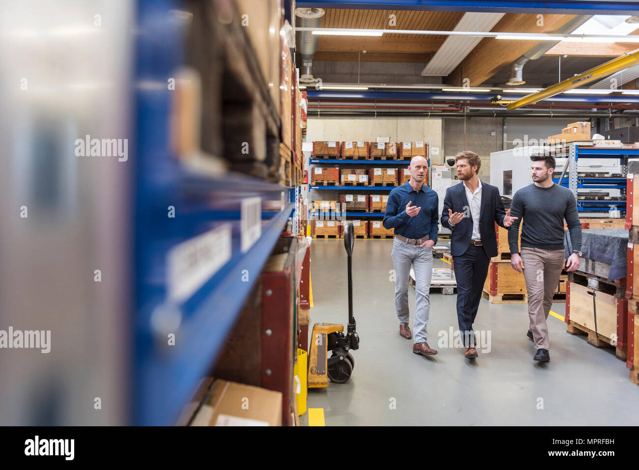 Three men walking and talking in factory storeroom Stock Photo
