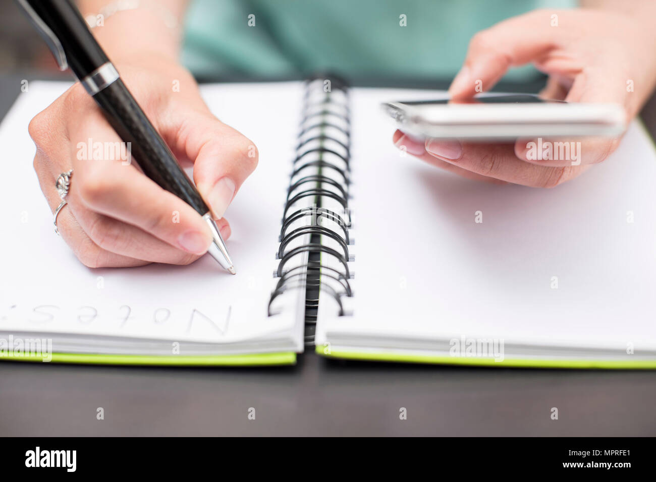 Woman writing notes in diary, holding smartphone Stock Photo