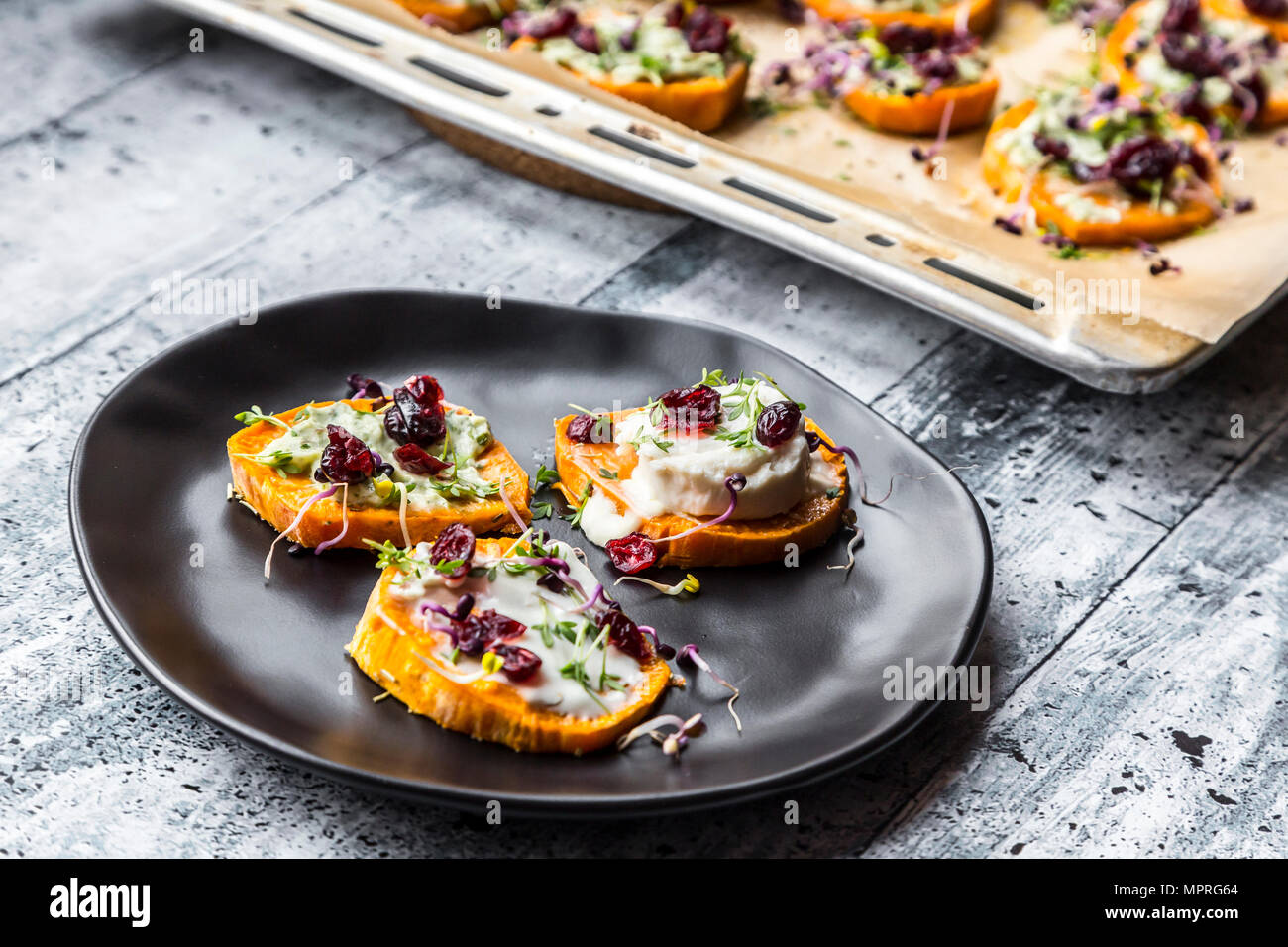 Slices of sweet potato with cream cheese, ramson cream, goat cheese, cress and cranberries Stock Photo