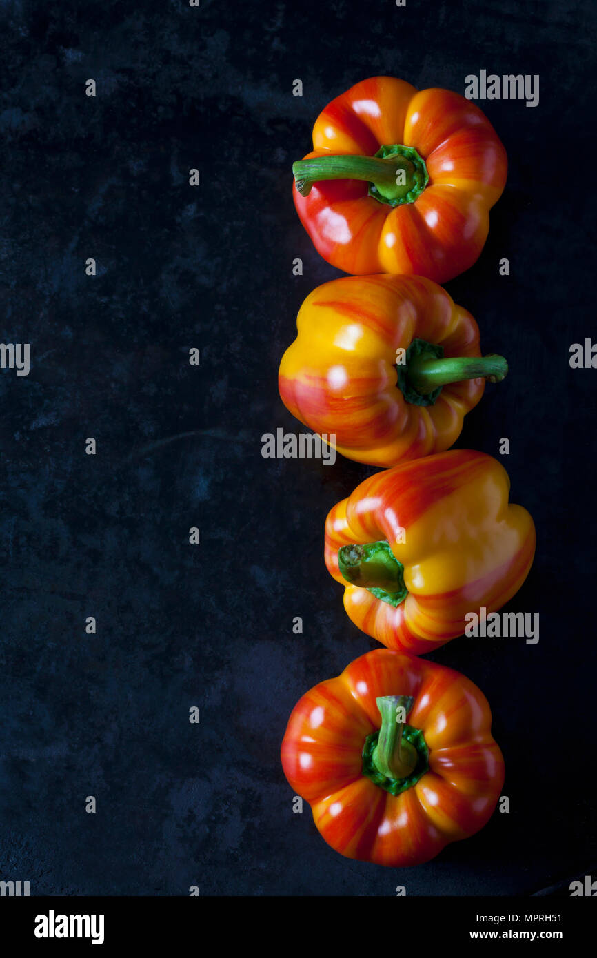 Row of four tiger bell peppers on dark metal Stock Photo