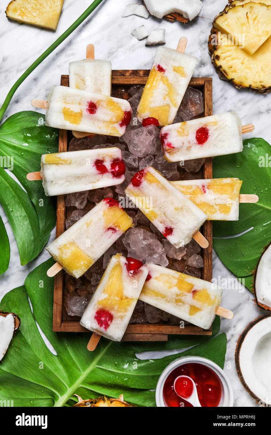 Pina Colada popsicles with candied cherries and pineapple on leaf Stock Photo