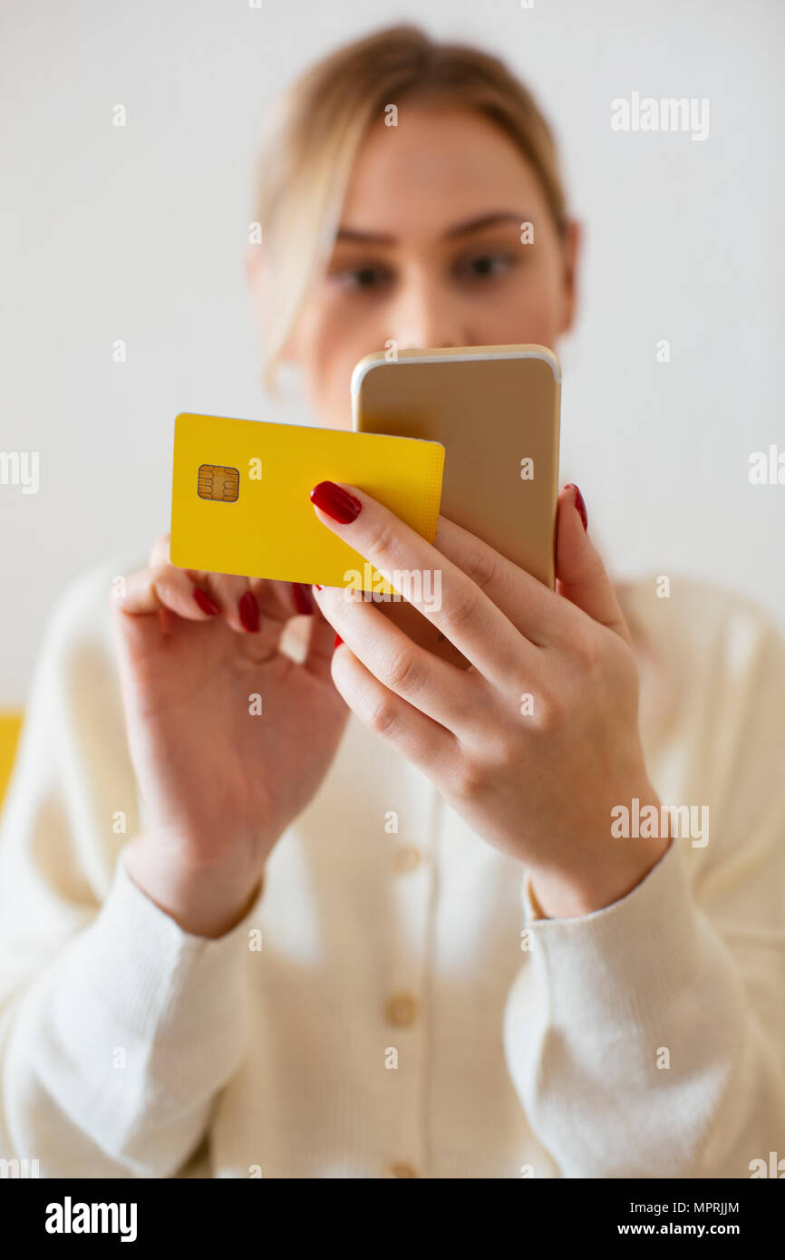 Blonde woman using smartphone and using bank card at home Stock Photo