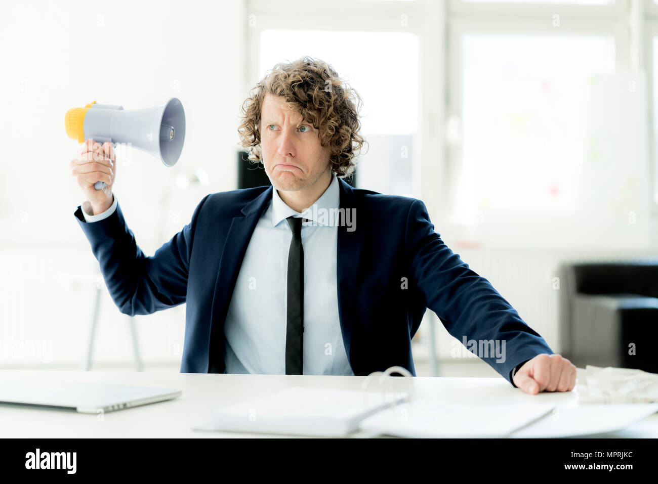 Businessman sitting in office trying out megaphone Stock Photo