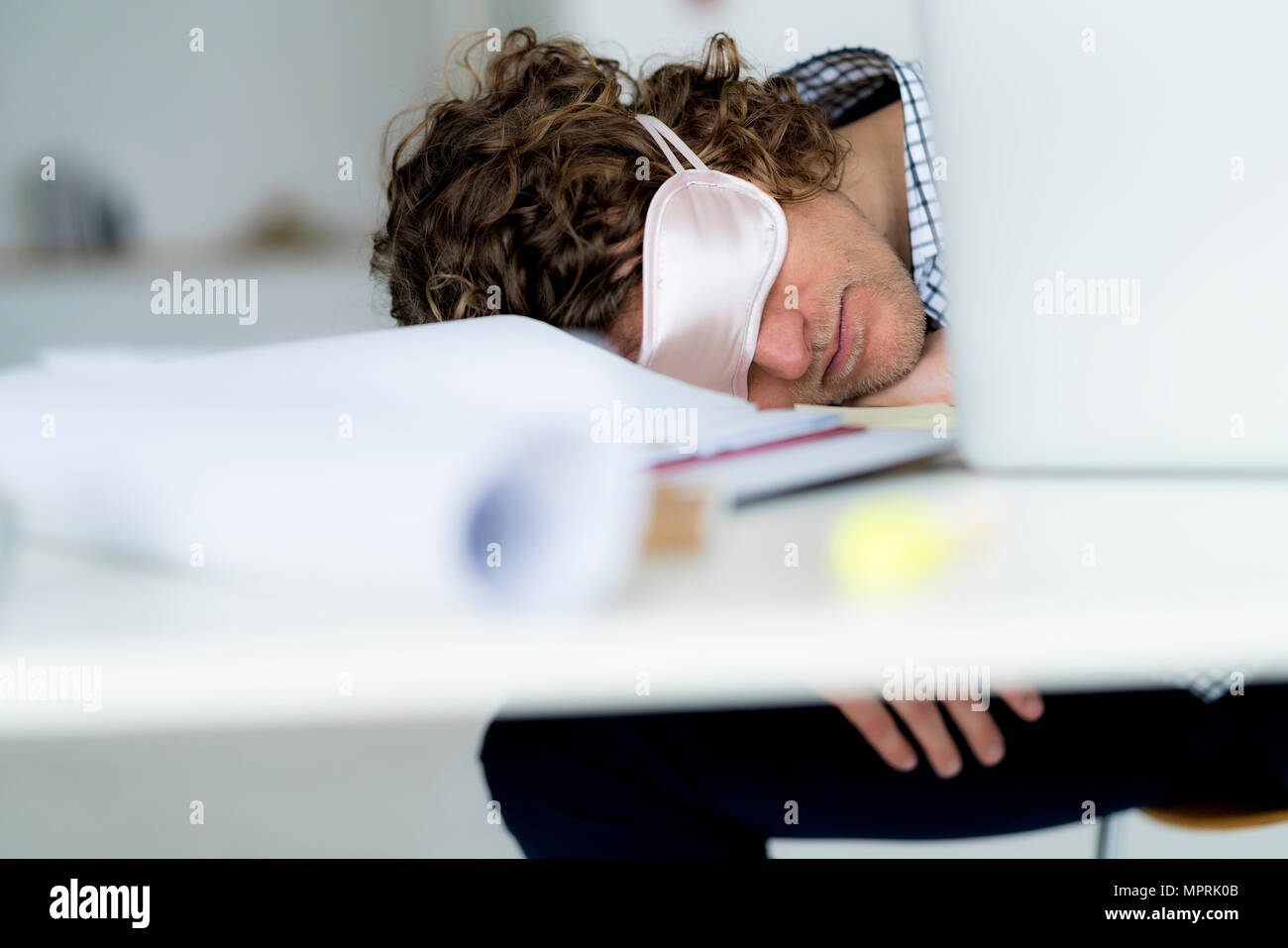 Overworked businessman sleeping at his desk wearing a sleeping mask Stock Photo