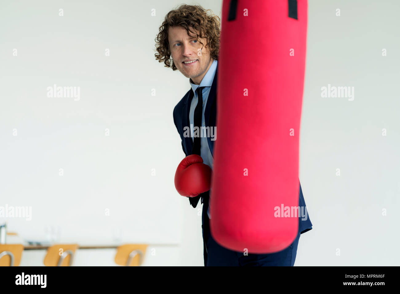 Stressed businessman hitting punch bag with boxing gloves in his office