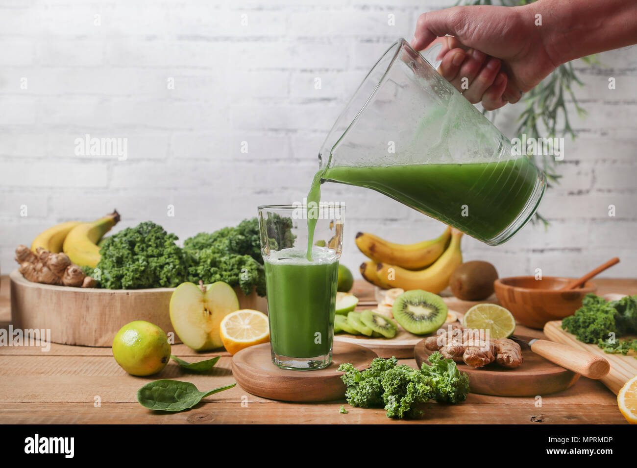 Man serving glass of green smoothie surrounded by ingredients Stock Photo