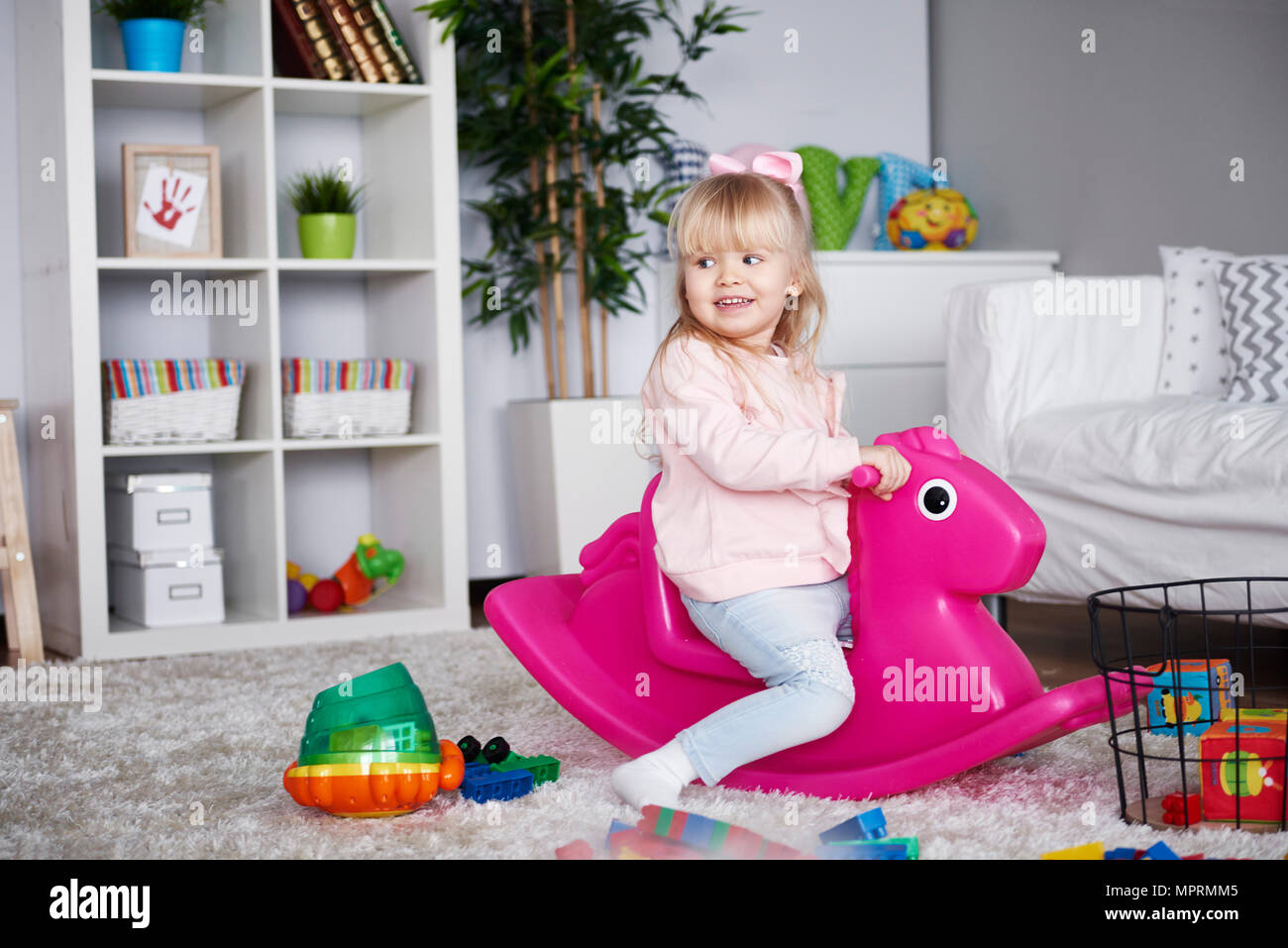 Portrait of smiling little girl sitting on pink rocking horse in the living room Stock Photo