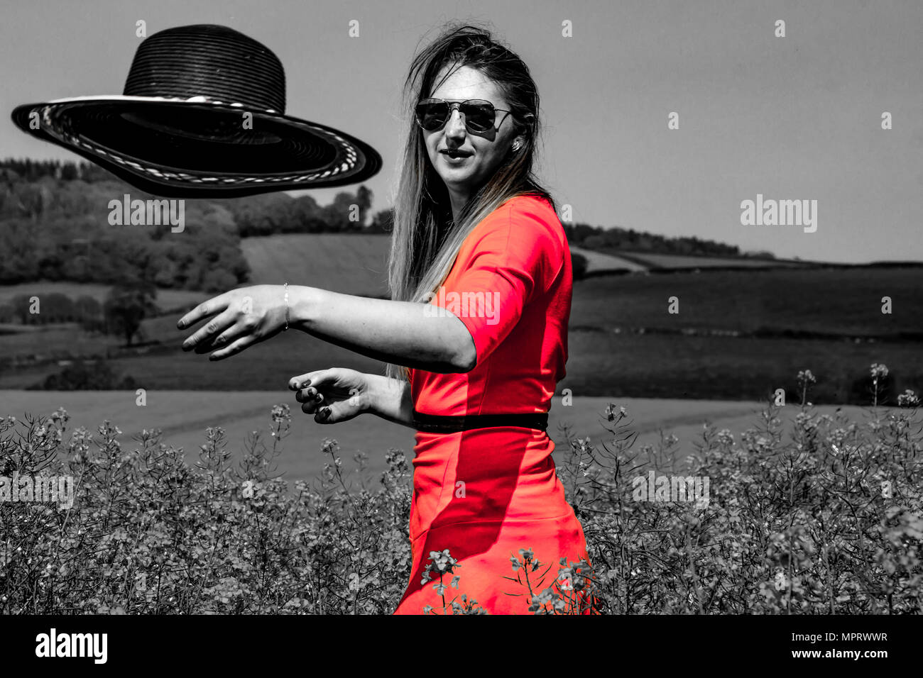 A young woman wearing a red dress in the yellow fields of rapeseed ...