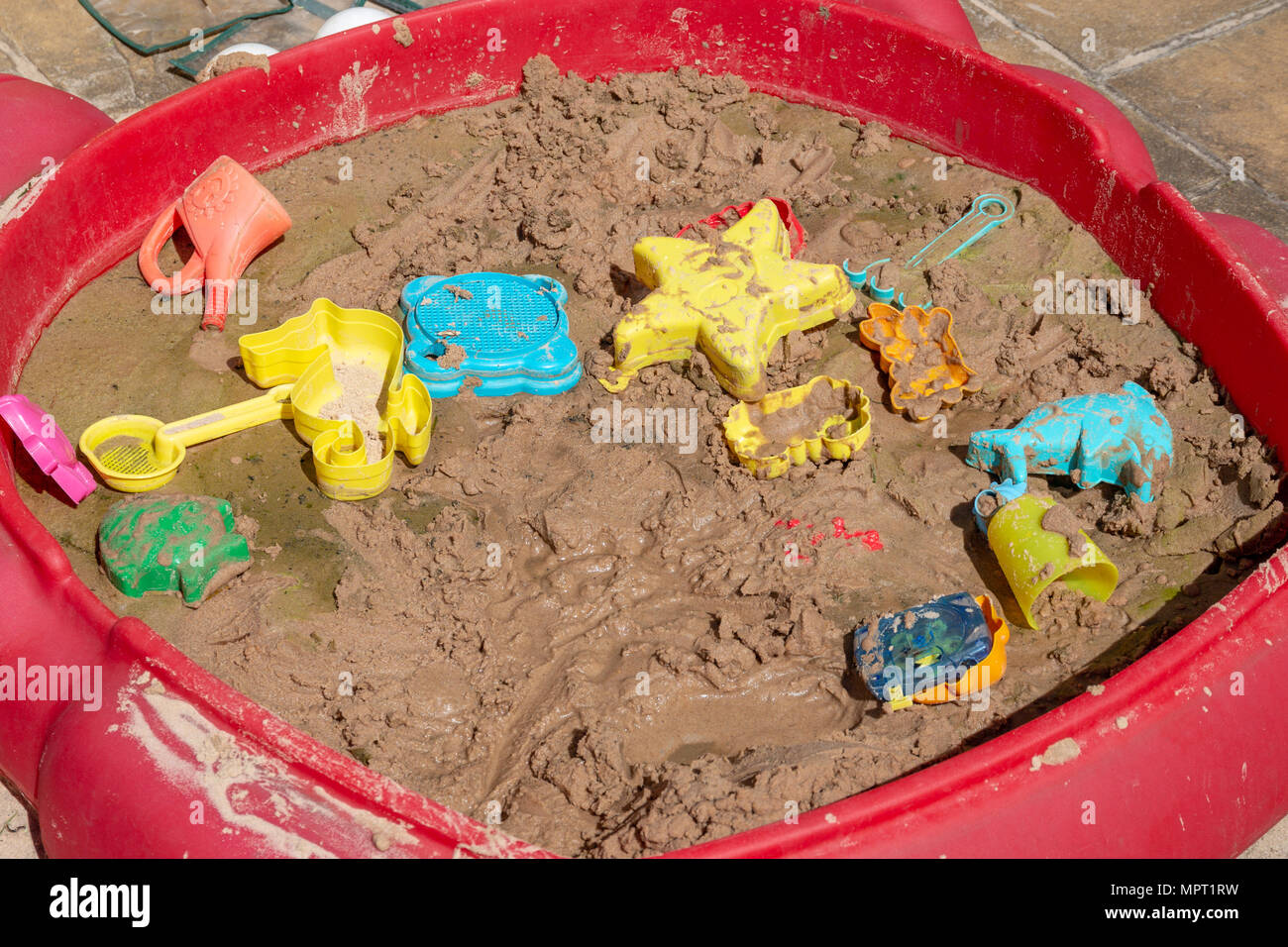 An untidy and unhealthy sandpit with sand toys, waterlogged with mould Stock Photo