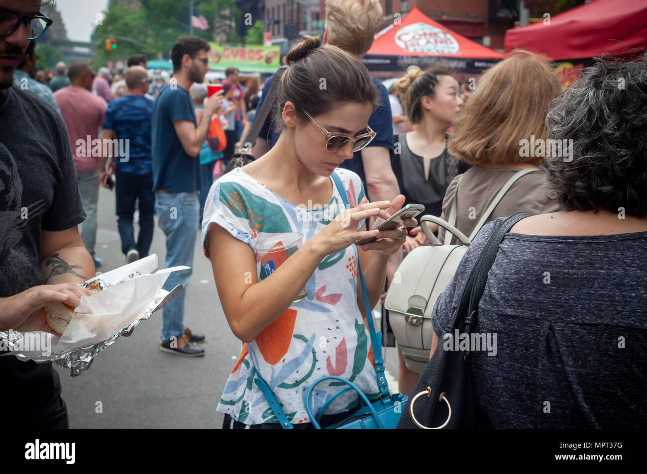 A millennial woman on her smartphone in the middle of the crowds at the 45th Annual Ninth Avenue International Food Festival in New York on Sunday, May 20, 2018. (Â© Richard B. Levine) Stock Photo