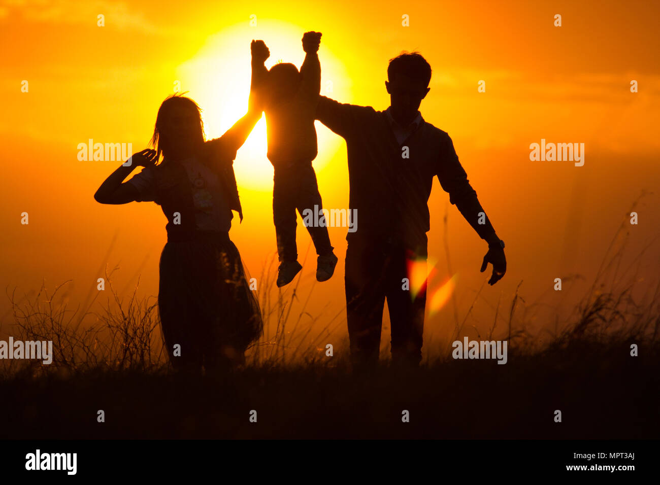 Silhouettes of a family of 3, who hold hands Stock Photo