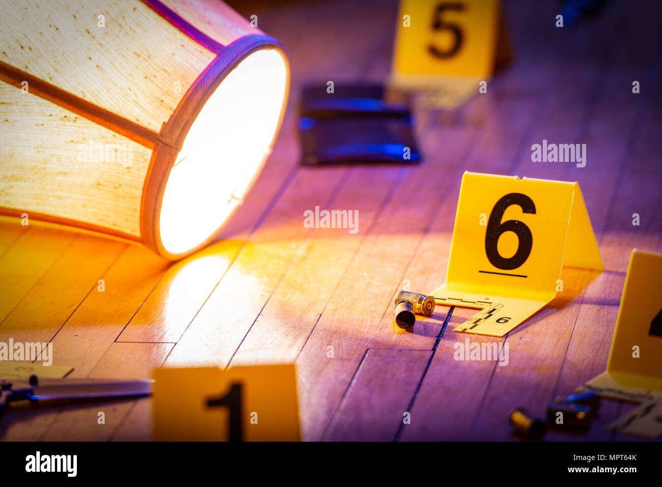 Evidence is marked with evidence markers on the floor of a home. A knocked over lamp lays nearby. Stock Photo