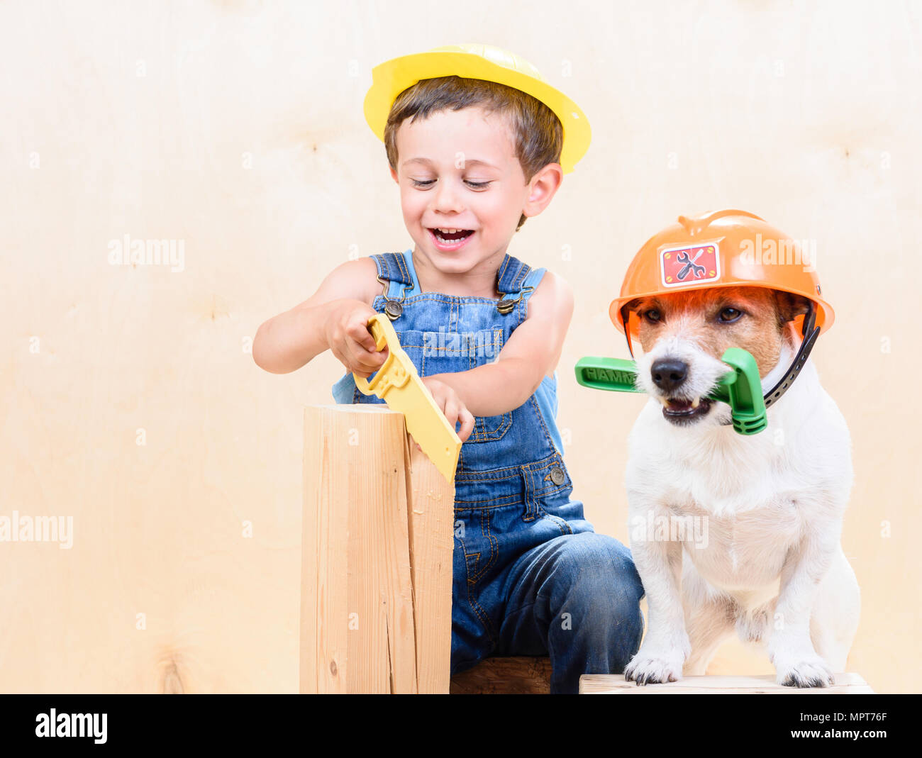 Kid and dog wearing hardhats working with saw and hammer at construction site Stock Photo