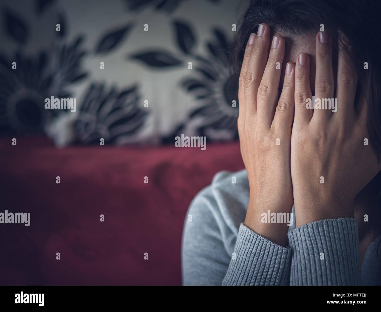 Closeup portrait of sad young woman sitting by sofa at home Stock Photo ...
