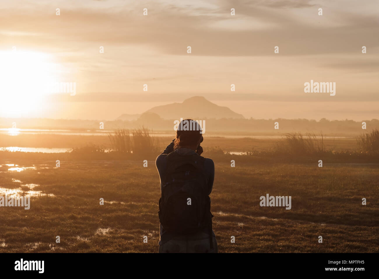 silhouette of a woman holding a smartphone taking pictures outside during sunrise or sunset. Stock Photo