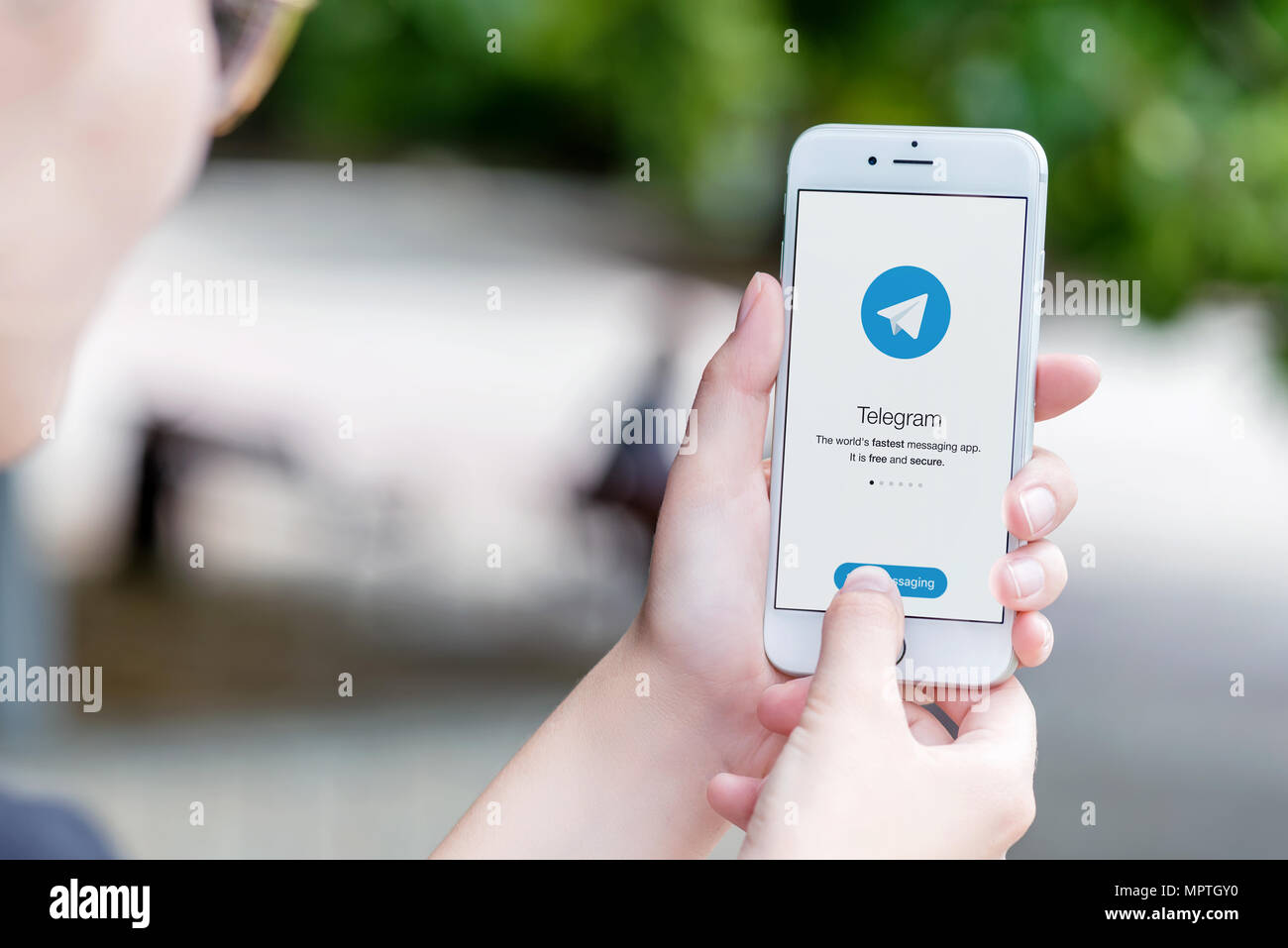 Telegram messenger on Apple iPhone in female hands over the shoulder view. Stock Photo
