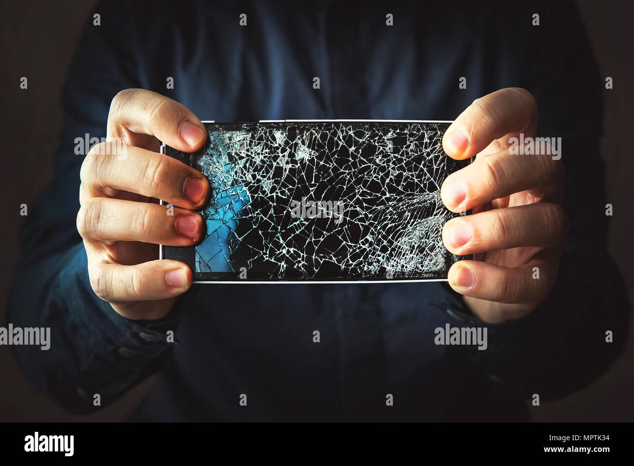 Broken phone screen in hand in dark background. Guy breaks a black modern frameless phone to which the screen cracks Stock Photo