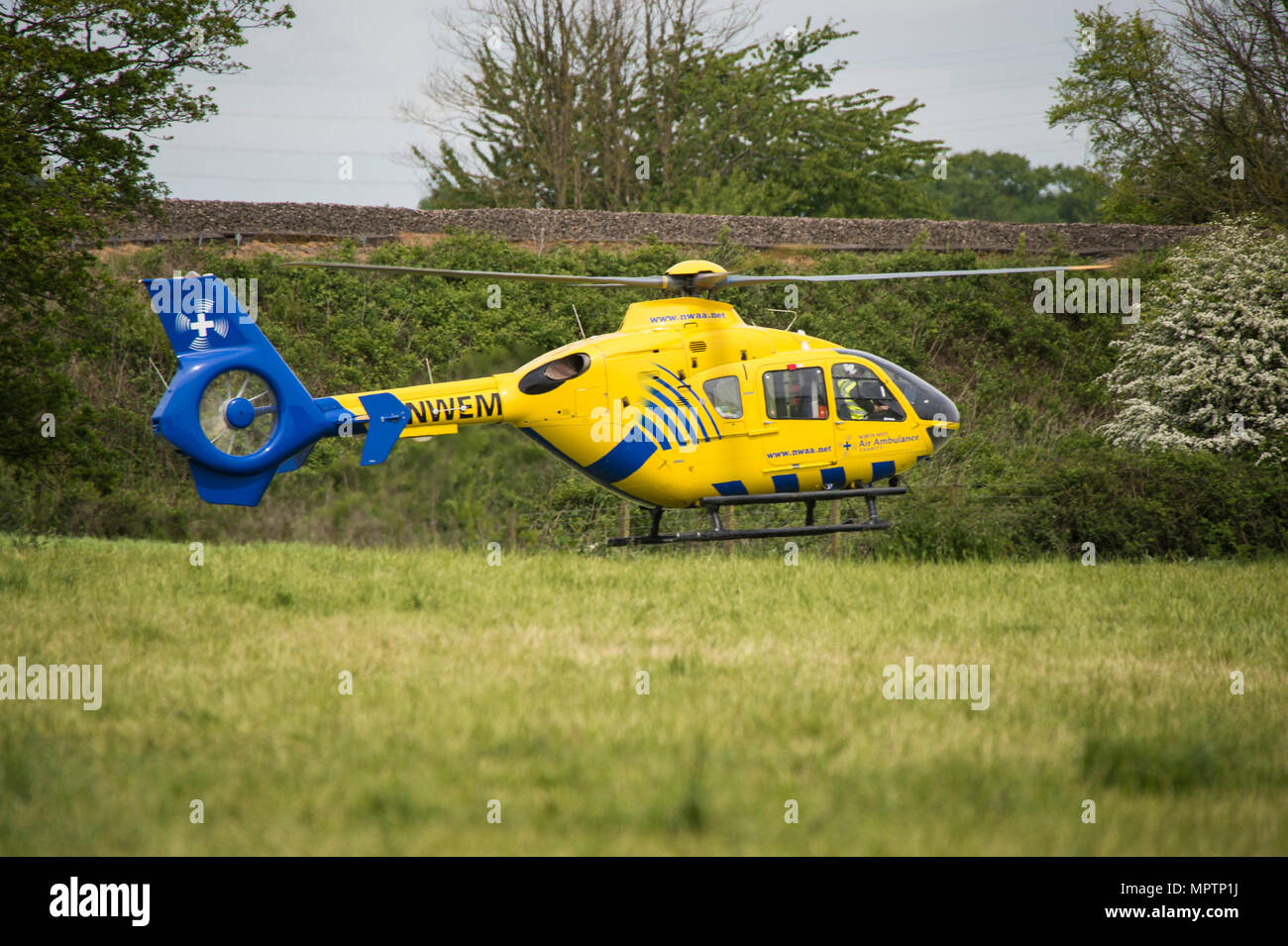 Yellow air ambulance helicopter landing in field next to motorway crash ...