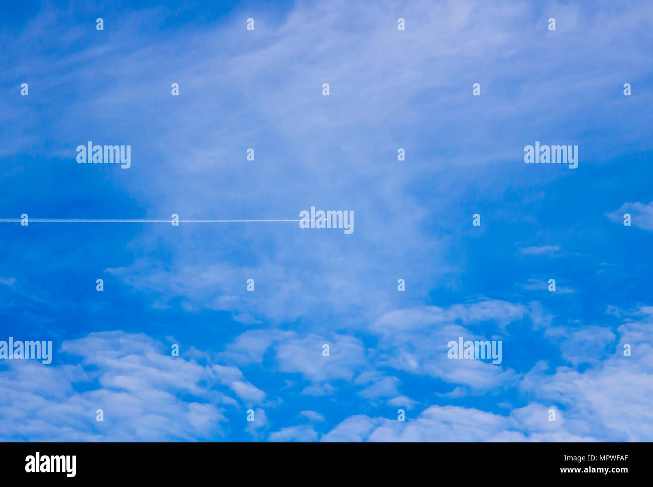 White Trace from airplane in blue sky with sparse clouds Stock Photo
