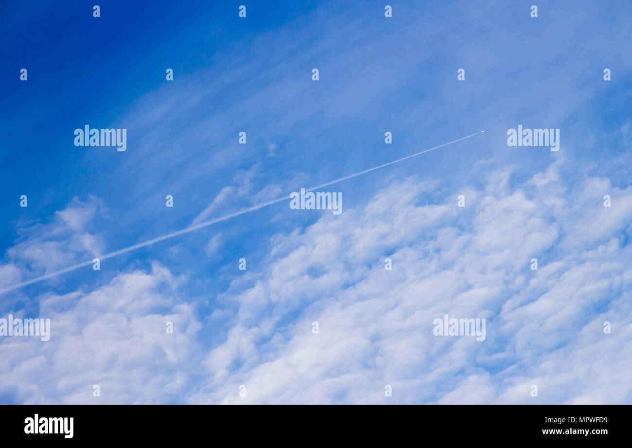 White Trace from airplane in blue sky with sparse clouds Stock Photo