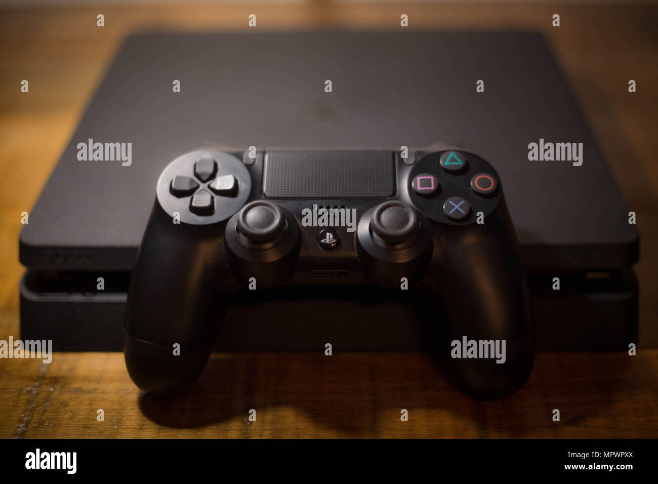A Sony PlayStation 4 video game console with a black wireless controller next to it. The PlayStation 4 or PS4 is knows as the eighth generation of home video game console developed by the Japanese company Sony Interactive Entertainment. The console sold for about 74 million units since it was released in November 2013. Stock Photo