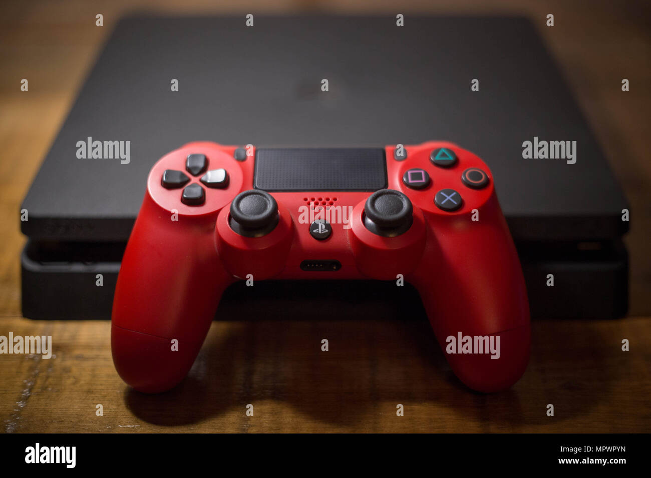 A Sony PlayStation 4 video game console with a red wireless controller next to it. The PlayStation 4 or PS4 is knows as the eighth generation of home video game console developed by the Japanese company Sony Interactive Entertainment. The console sold for about 74 million units since it was released in November 2013. Stock Photo