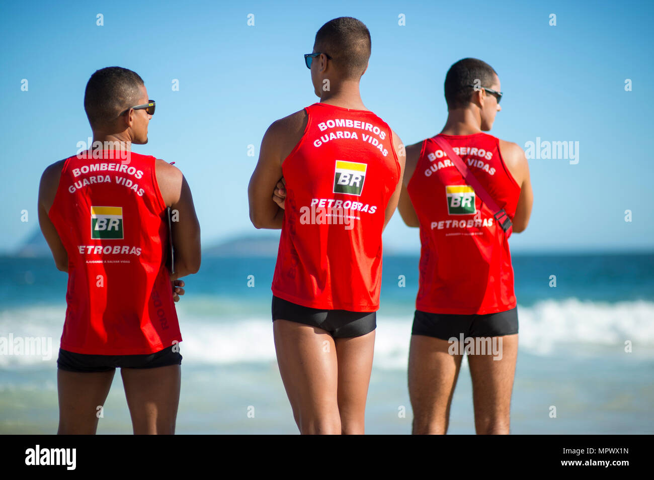 RIO DE JANEIRO - CIRCA MARCH, 2018: Group of three athletic life guards in uniform watch the heavy surf on Ipanema beach. Stock Photo