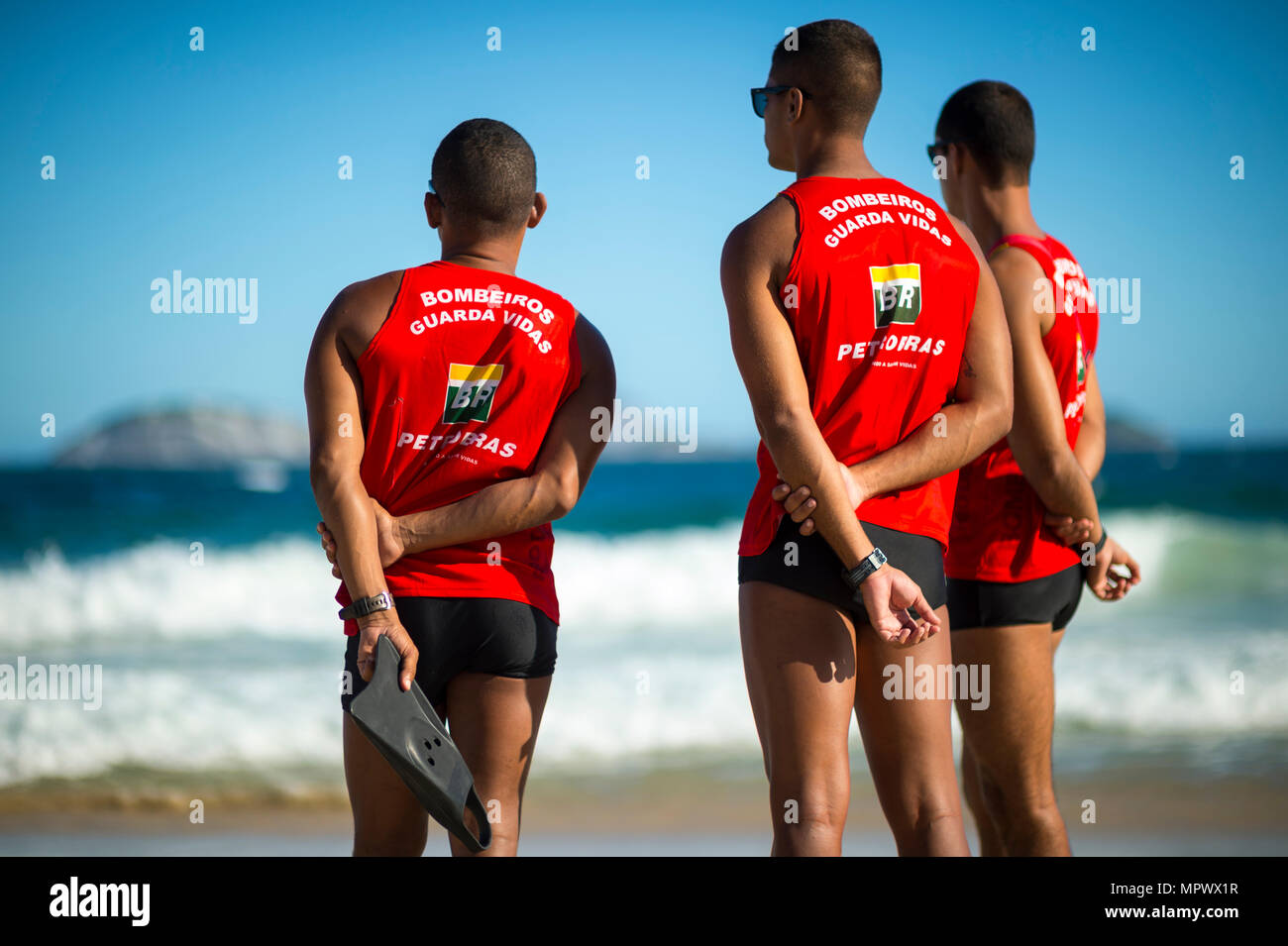 RIO DE JANEIRO - CIRCA MARCH, 2018: Group of three athletic life guards in uniform watch the heavy surf on Ipanema beach. Stock Photo