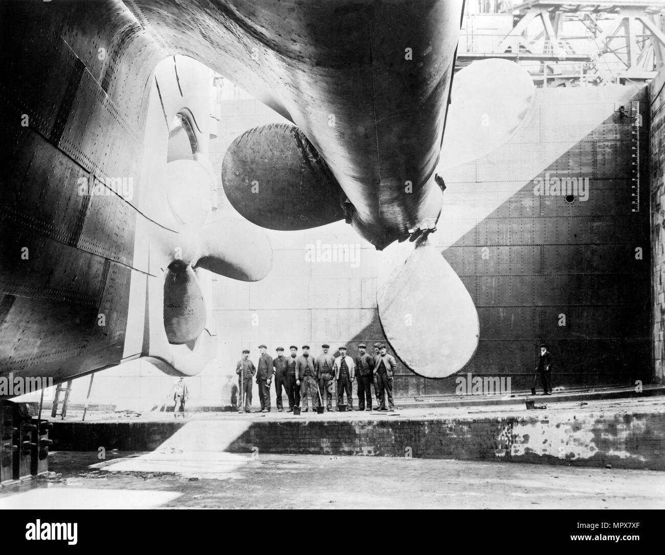Workmen standing under one of the propellors of the Titanic, 31 May, 1911 (b/w photo) Stock Photo