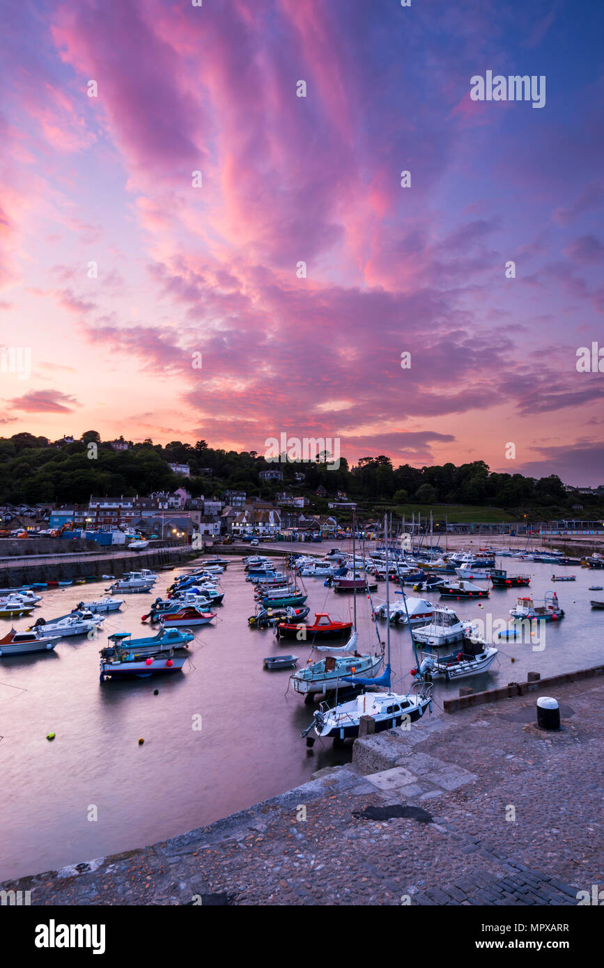 At sunset pink and red hues reflect off the clouds above the boat filled Cobb harbour at Lyme Regis on the Jurassic Coast of Dorset on 23rd May 2018. Stock Photo
