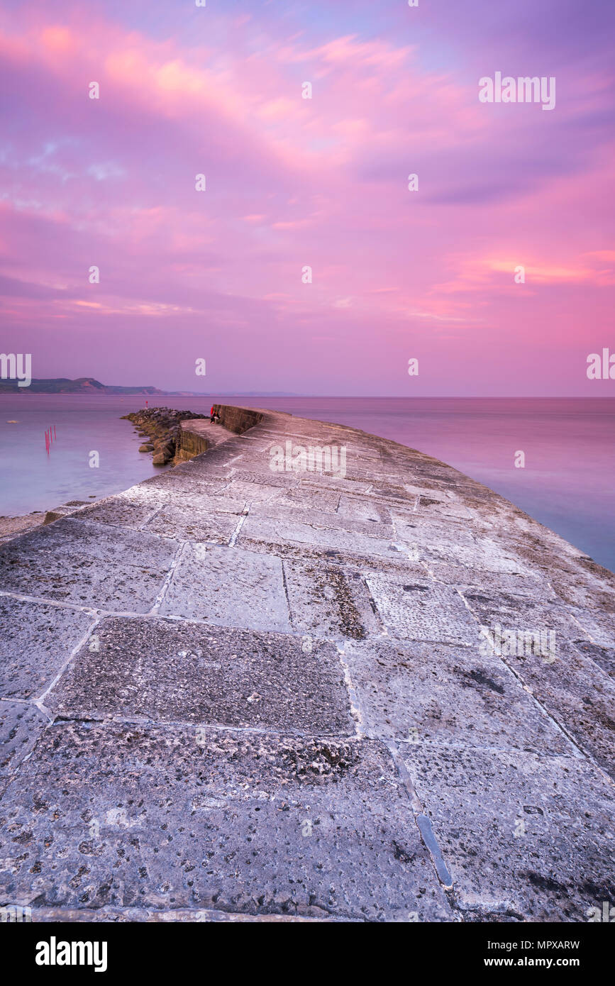 Pinks clouds in the sky at The Cobb harbour wall at Lyme Regis on the Jurassic Coast of Dorset at sunset on 23rd May 2018.  Picture Credit: Graham Hun Stock Photo