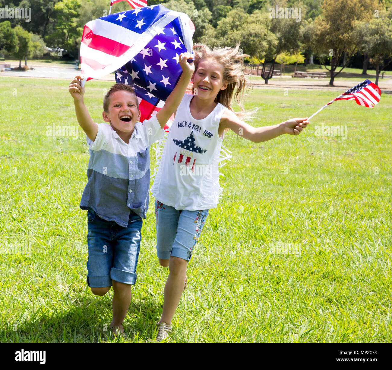 Little smiling patriotic girl with long blond hair,and boy holding an american flag waving in the wind outdoors on beautiful summer day. National 4 ju Stock Photo