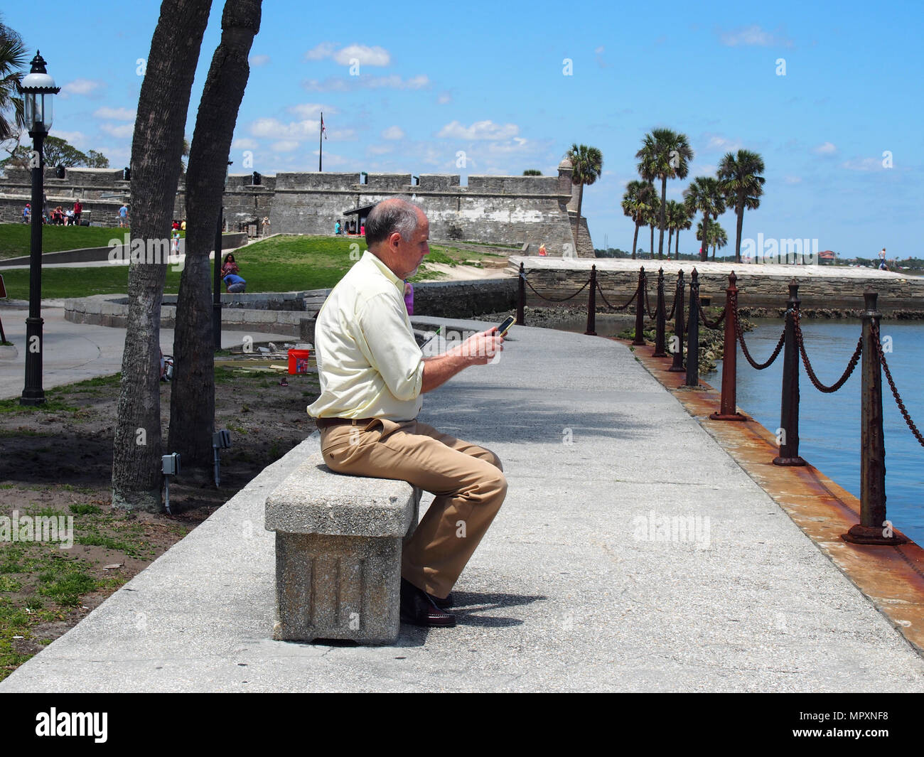 Man uses his smartphone while sitting on a bench along the Matanzas Bay in St. Augustine, Florida, USA, 2018, © Katharine Andriotis Stock Photo