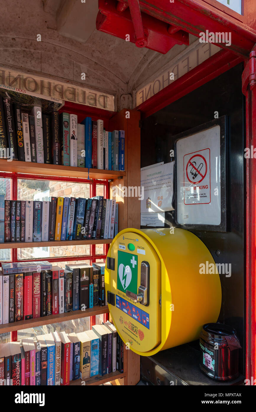 Red K2 telephone box used as a library and defibrillator station outside The Hatton Arms public house in Hatton, Cheshire, England, UK Stock Photo