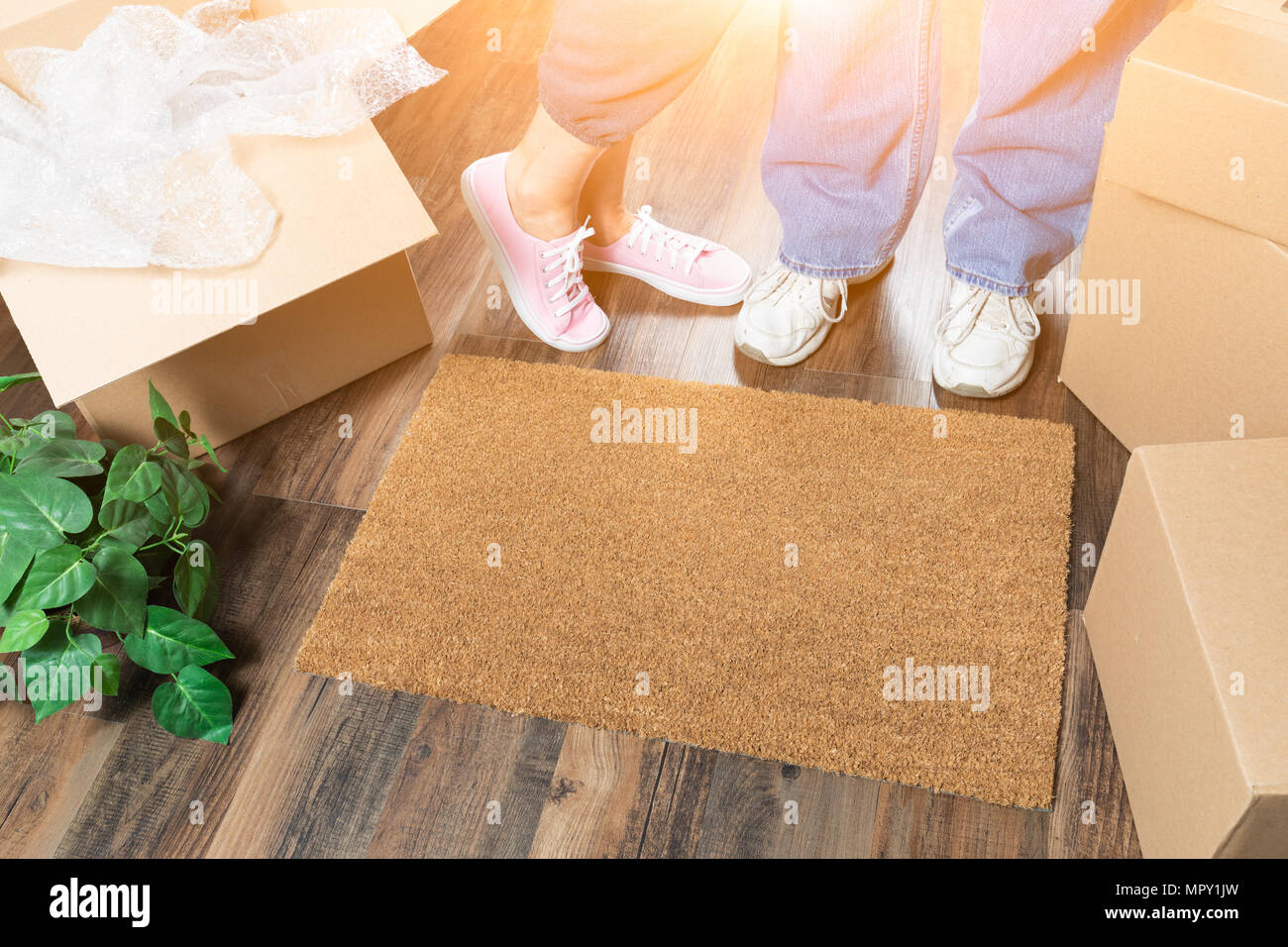 Man and Woman Standing Near Home Sweet Home Welcome Mat, Moving Boxes and Plant. Stock Photo