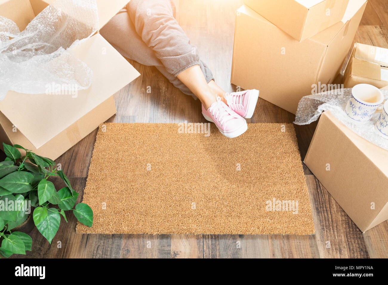 Woman Wearing Sweats Relaxing Near Home Sweet Home Welcome Mat, Moving Boxes and Plant. Stock Photo