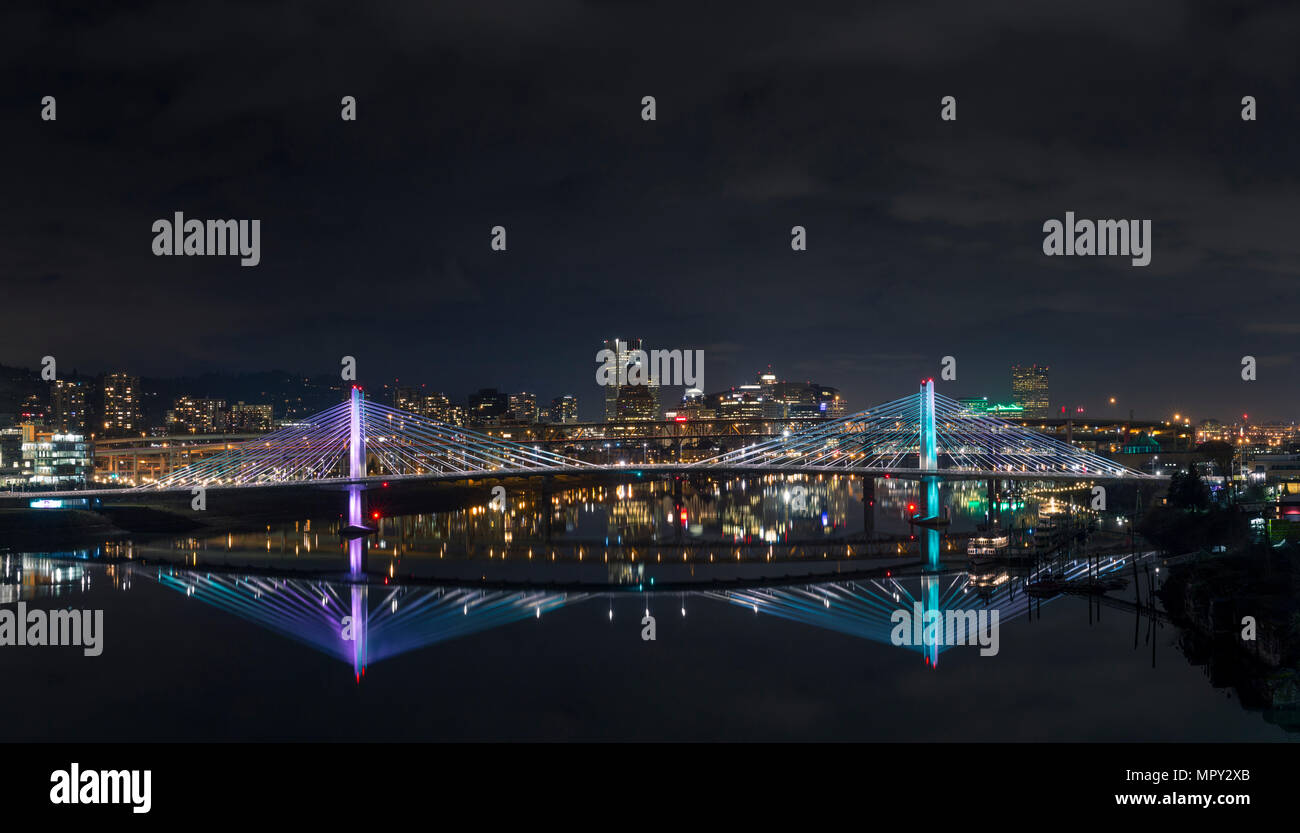 Reflection of illuminated city and bridge in river against sky at night ...