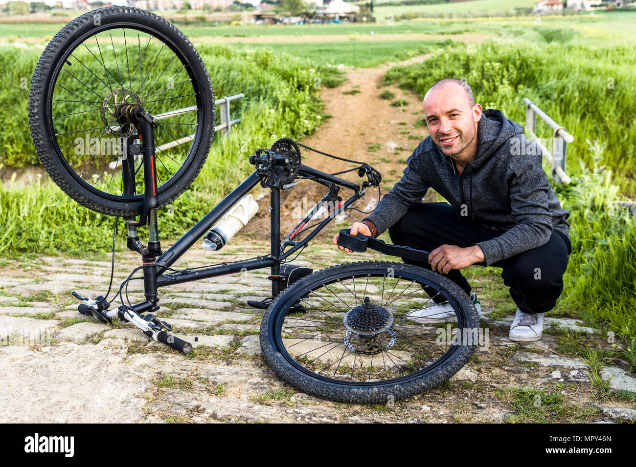 Portrait of man repairing bicycle on field against farm Stock Photo
