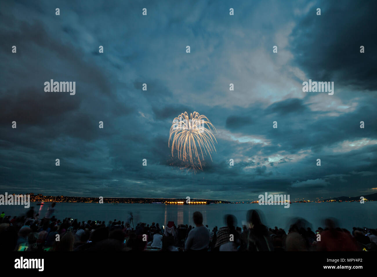 People enjoying firework display against cloudy sky over river at night Stock Photo