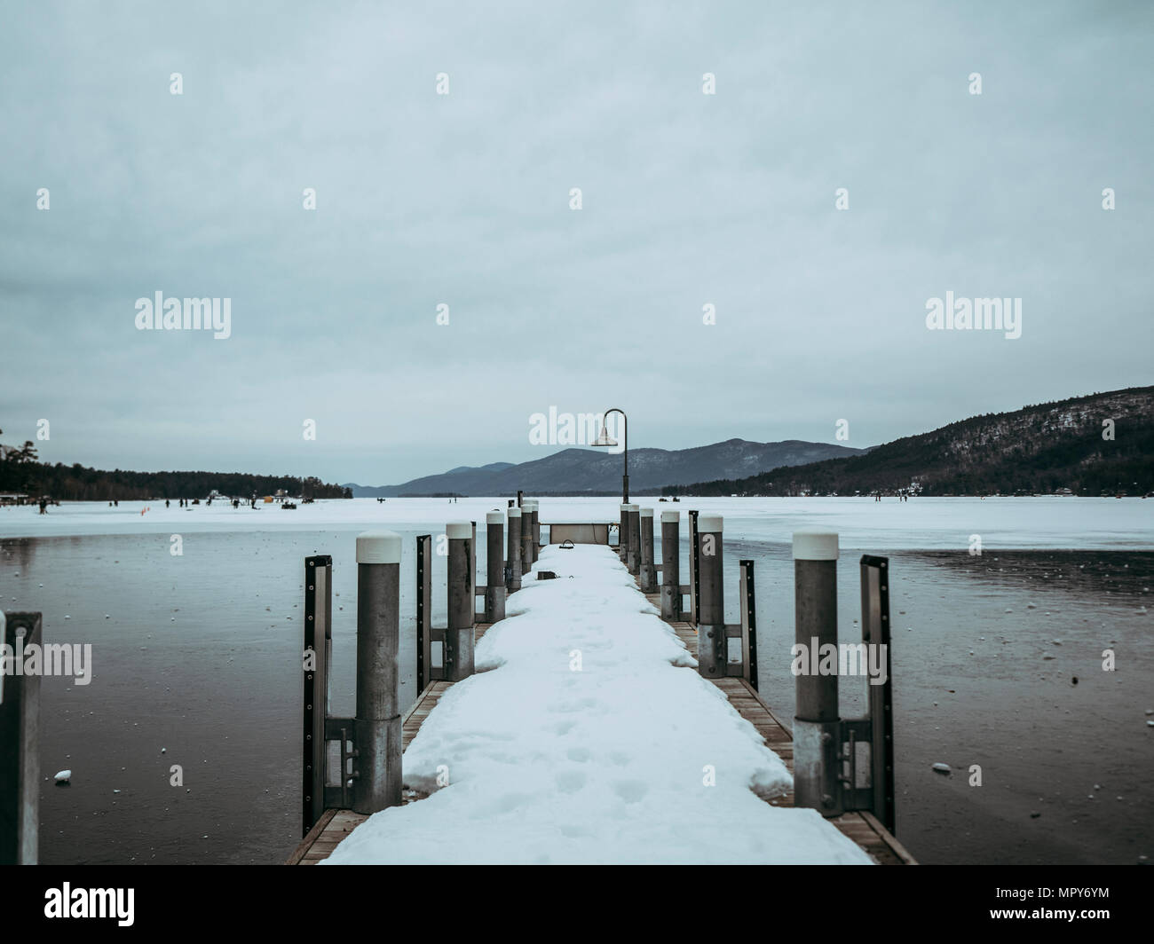 Snow covered pier over frozen Lake George against cloudy sky Stock Photo