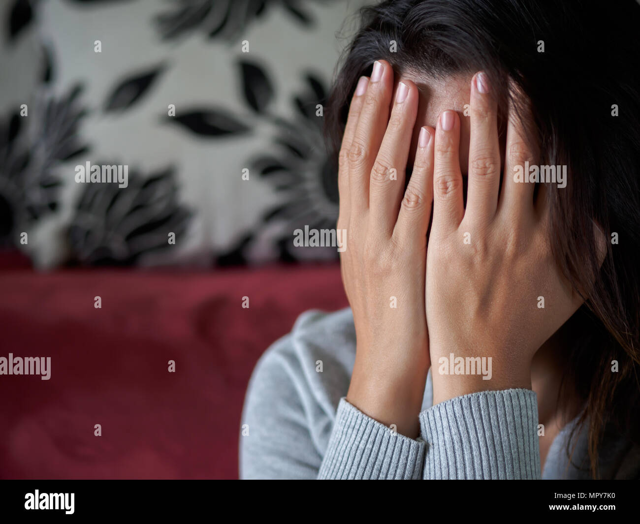 Closeup portrait of sad young woman sitting by sofa at home Stock Photo ...