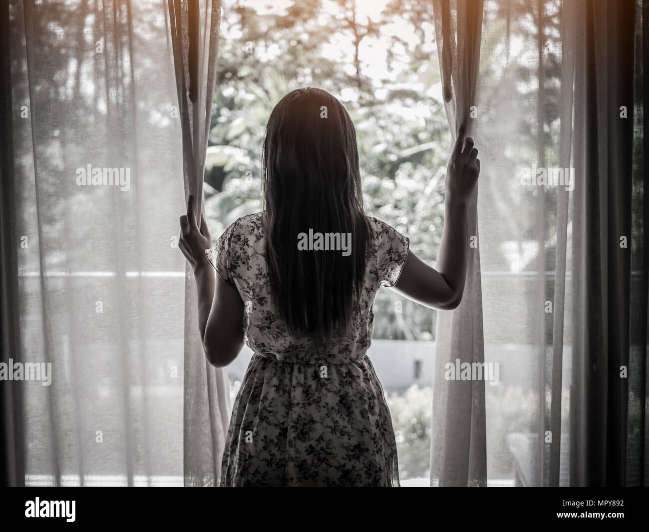 Rear view of a young woman holding the curtains open to looking