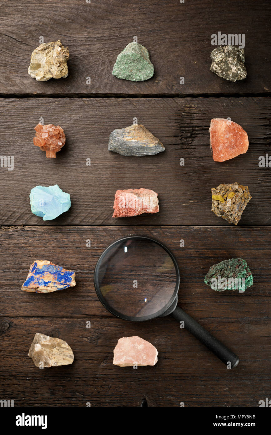 Overhead view of colorful gemstones with magnifying glass on wooden table Stock Photo