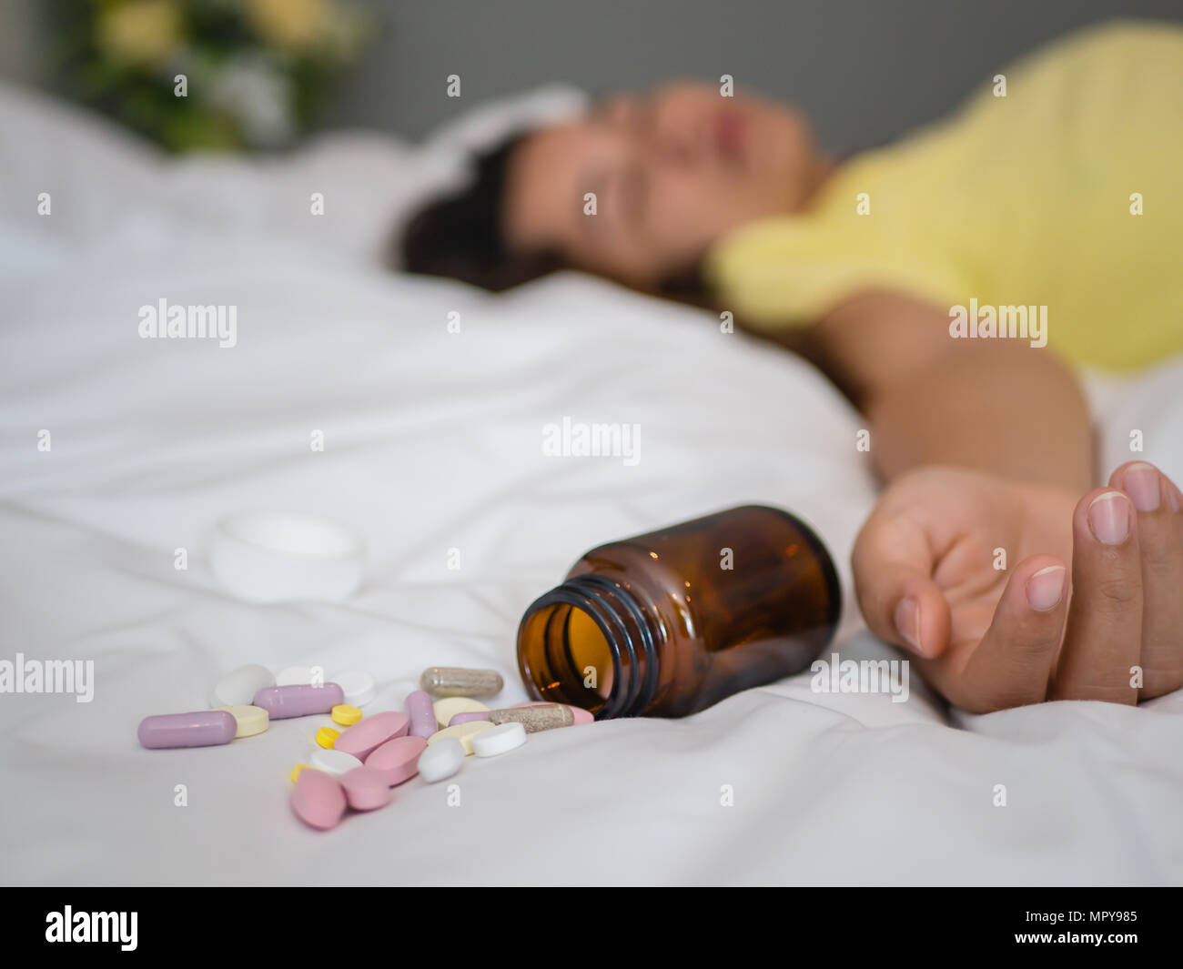 Young woman is lying on the bed with a lot of pills. Overdose and suicide concept. Stock Photo