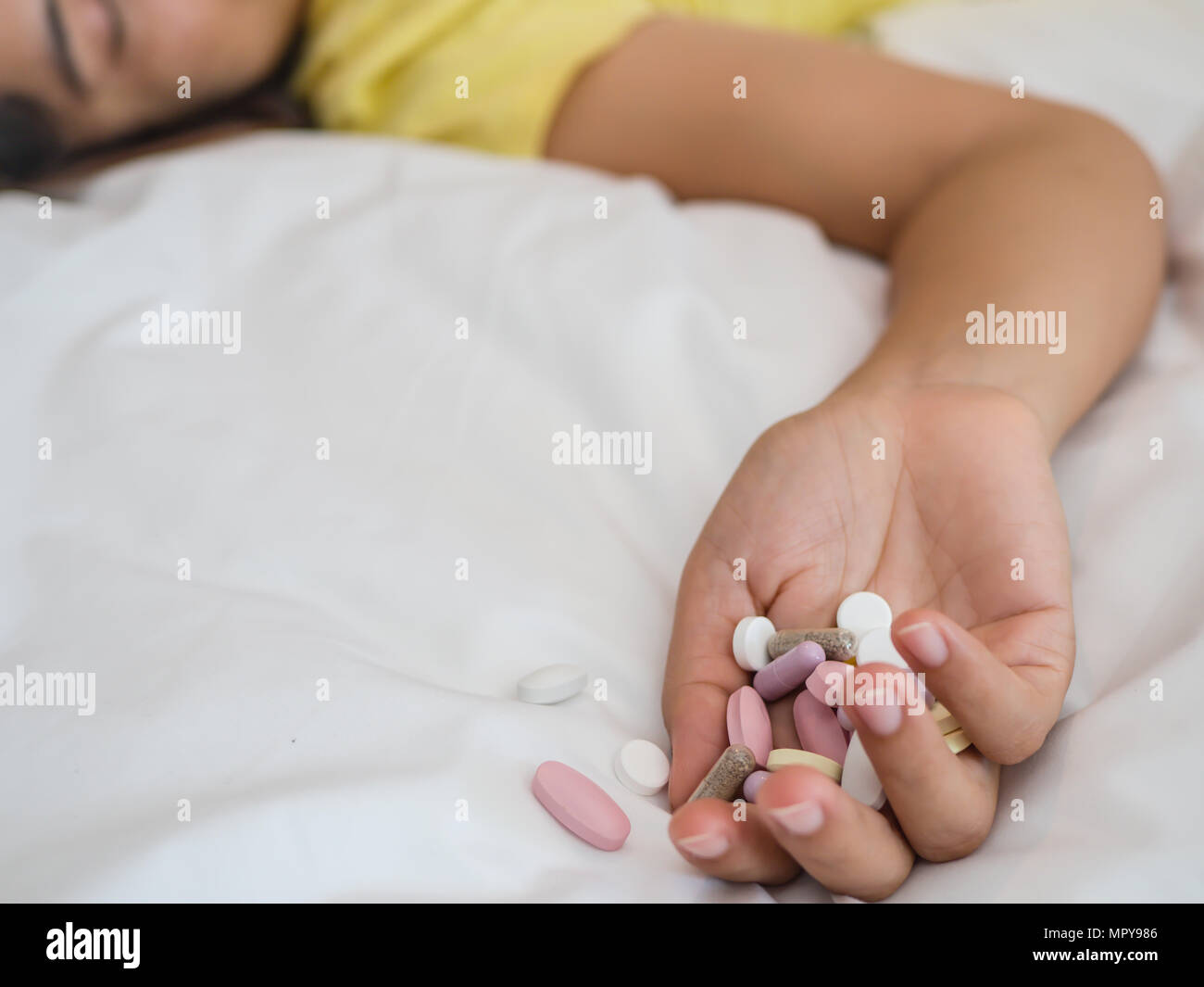 Young woman is lying on the bed with a lot of pills. Overdose and suicide concept. Stock Photo